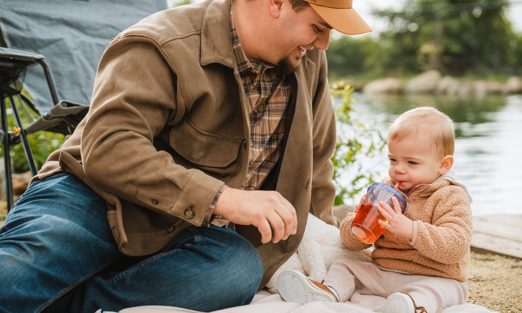 young father and baby daughter sitting outside by a lake