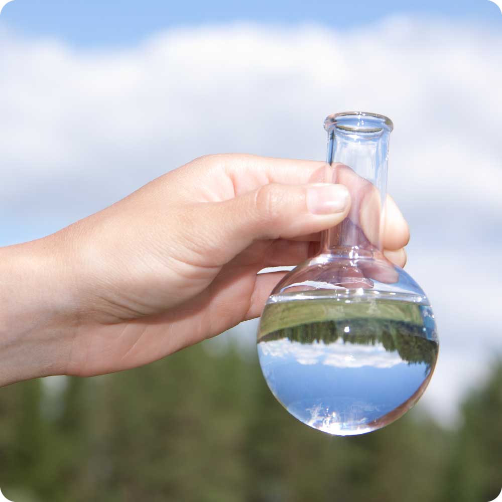 beaker of clear fluid and reflection of trees and blue sky