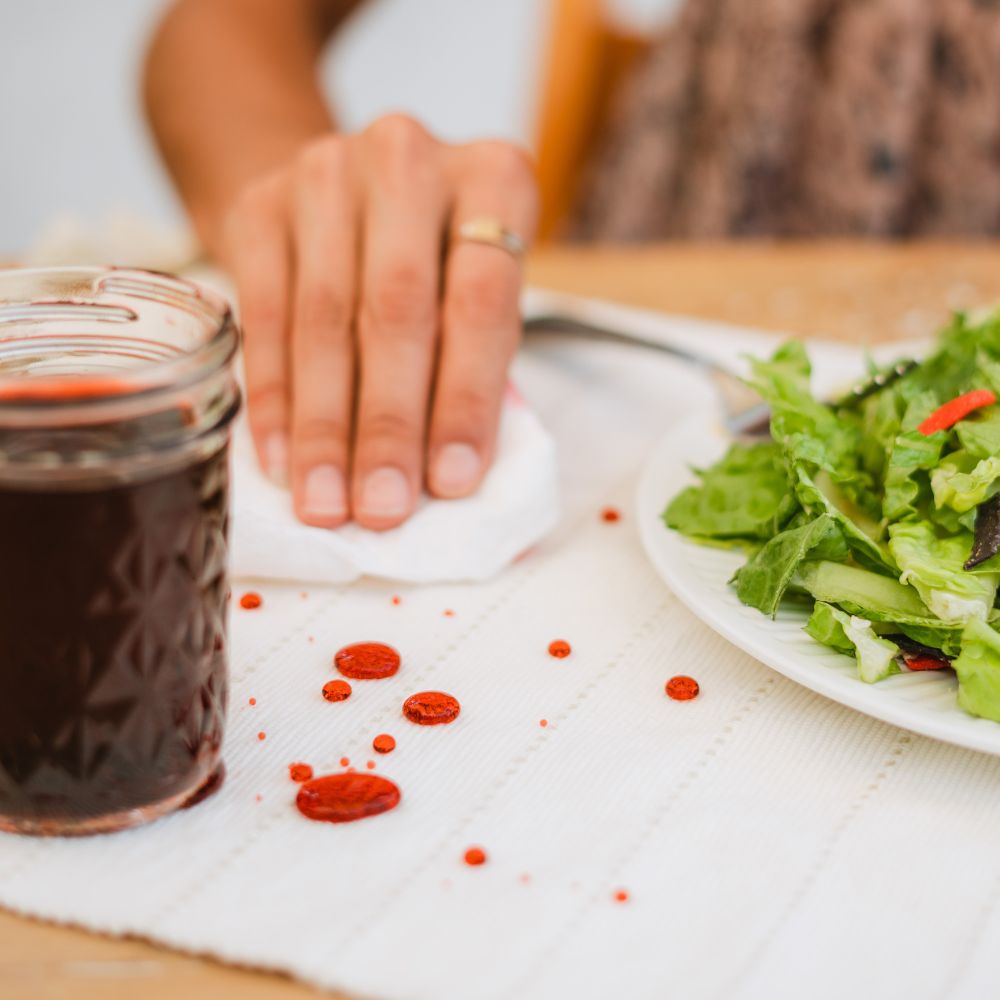 lady dabbing up cranberry juice that has beaded up on a protected fabric table placemat