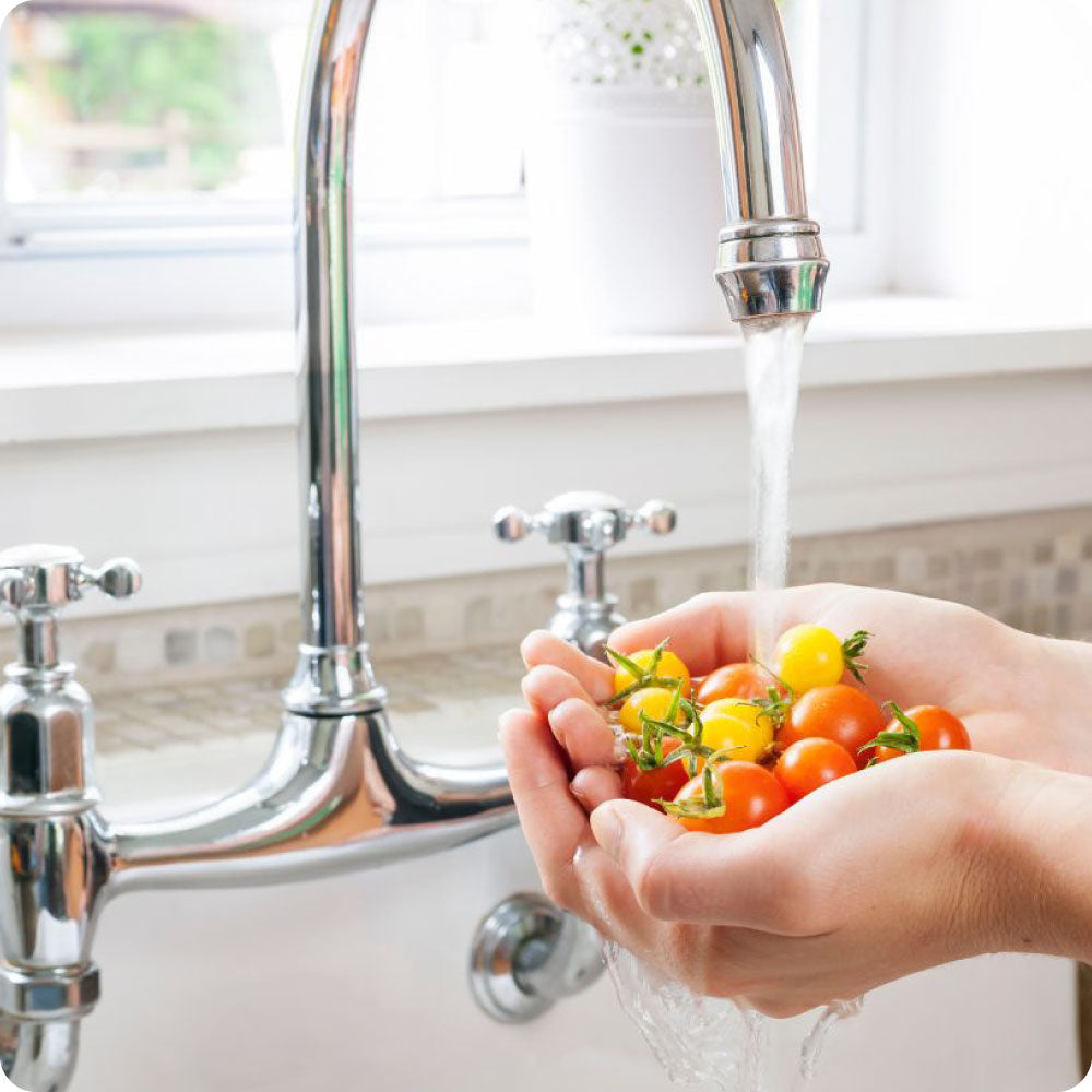 hands washing tomatoes in a kitchen sink